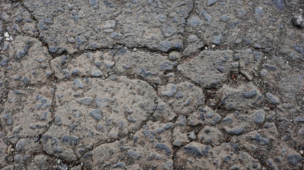 Damaged asphalt road, cracked cracks and scattered stones, with selective focus