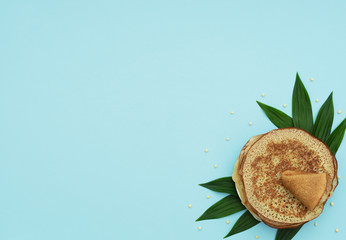 Fototapeta na wymiar Homemade pancakes on blue background with green leaves and beads. Maslenitsa, spring festival concept. Russian traditional food. Pancake week. Delicious breakfast. Flat lay style with copy space.