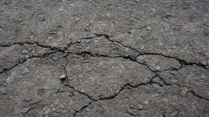Damaged asphalt road, cracked cracks and scattered stones, with selective focus
