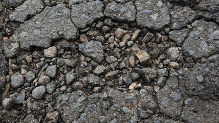Damaged asphalt road, cracked cracks and scattered stones, with selective focus