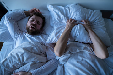 Woman is stressed, covers her face with a pillow, she cannot fall asleep because her husband...