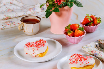 Party table with heart shaped donuts, strawberry and tea.
