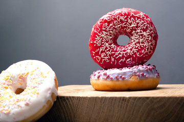 multicolored holiday donuts powdered on a wooden stand on a gray background. glaze of red white and violet color