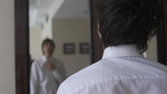 Young man dressing himself in front of mirror.