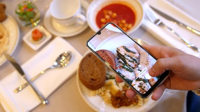 Male hands using smartphone taking photos of chicken pasta with tomato coup and slice of bread