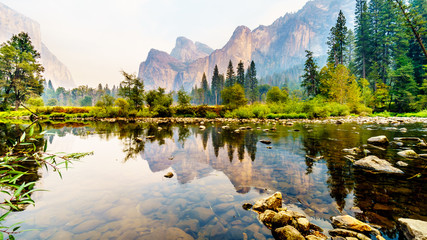Reflections of Cathedral Rocks, Taft Point and Sentinel Dome in the Merced River in the smoke filled Yosemite Valley due to the 2019 Briceburg Fire outside Yosemite National Park California, USA - obrazy, fototapety, plakaty