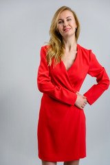 Model Standing in a red dress right in front of the camera. Vertical portrait of a beautiful woman 38 years old blonde on a white background with a smile.