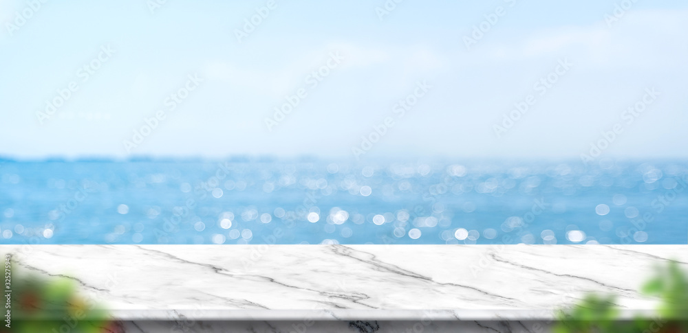 Poster empty white marble table with blur blue sky and sea bokeh background with green leaf foreground,mock