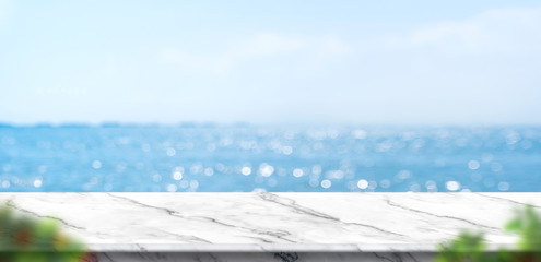 Empty white marble table with blur blue sky and sea bokeh background with green leaf...