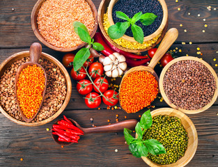 Wooden bowls of various lentils with red and green hot chilli peppers with leaves and tomatoes on a wooden background. Top view.