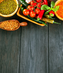 Wooden bowls of various lentils with red and green hot chilli peppers with leaves and tomatoes on a wooden background. Top view. Text space.