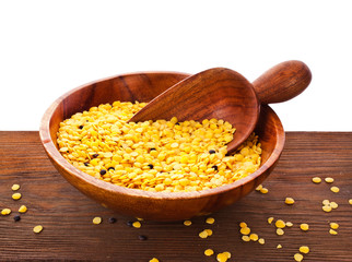 Wooden bowl of yellow lentils with scoop on a wooden background.