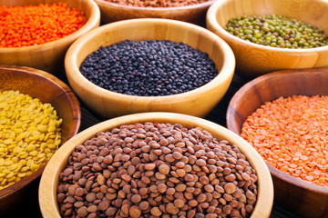 Wooden bowls of various lentils on a wooden background.