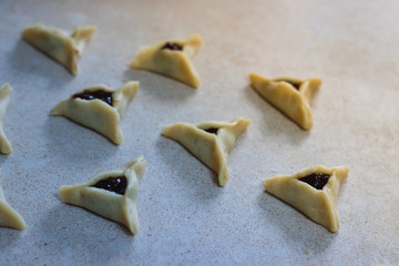 Fototapeta na wymiar Hamantaschen. (ozenei haman) Triangular pastry made of crispy dough, stuffed with chocolate. For the Jewish holiday of Purim. Handmade in the middle of preparation, dough triangles ready for baking.