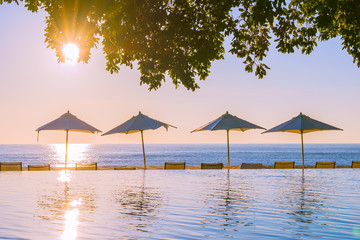 Beautiful tropical outdoor beach sea ocean with umbrella and chiar around outdoor swimming pool at sunset or sunrise time