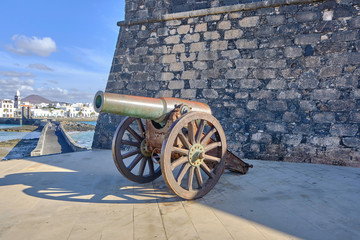 Fototapeta na wymiar Scenic view of old cannon near walls Castle of San Gabriel (Castillo de San Gabriel) in Arrecife on Lanzarote island in Canary islands in Spain. Beautiful summer cloudy look of old gun near fort