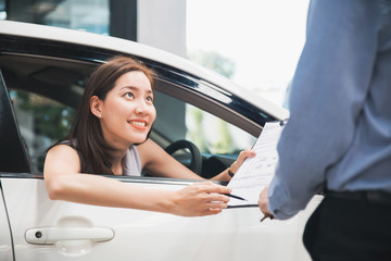 Car Dealership. The Asian woman checking a checklist with a smile for the salesman before hand...