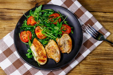 Fried chicken breast with salad of fresh arugula and cherry tomatoes on wooden table. Top view