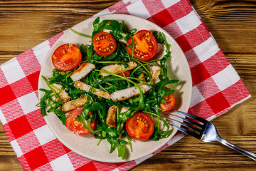 Tasty salad of fried chicken breast, fresh arugula and cherry tomatoes on wooden table. Top view