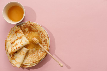 Delicious homemade pancakes with honey on a gently pink background. Top view, close-up. Traditional holiday celebration concept. Russian translation wide and happy Shrovetide Maslenitsa.