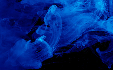 Fototapeta premium Blue watercolor ink in water on a black background. Colored space background.