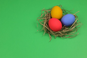 Three painted chicken eggs red blue and yellow lie in a nest made of straw on a green background. The Easter theme.  Selective focus