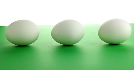 Three white chicken eggs lie on a green tabletop in the room.  Selective focus
