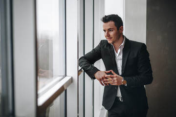 Successful and respectable man looks out the window in the office and leaned on his elbow