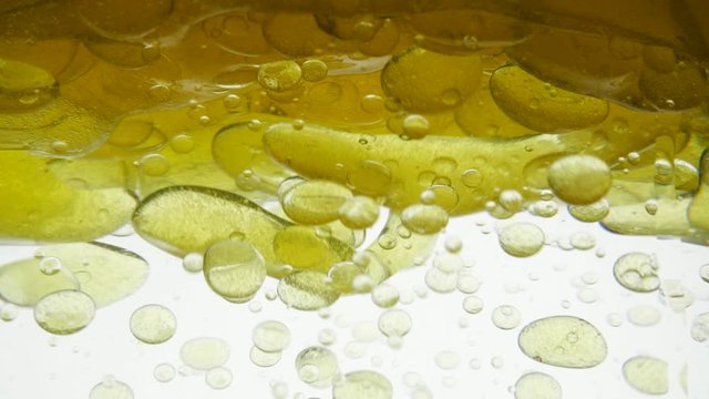 Bright colored air bubbles on background of golden oil. Yellow liquid is poured into a container, close-up view. Different density of the liquid, fat molecules do not mix with water. Focus boiling oil
