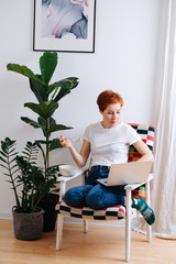 Woman with short ginger hair eating muesli in a chair at home while browsing