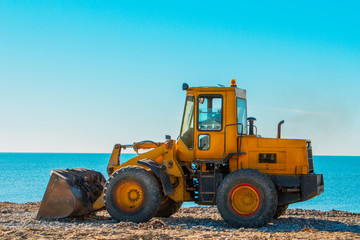 Yellow bulldozer on the background of clear blue sky and seashore. Close up