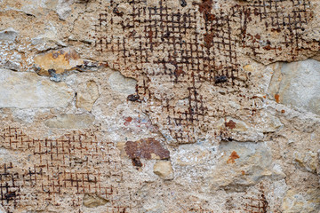 Old wall with partially crumbling plaster with incoming supporting metal mesh