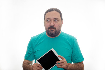 An untidily dressed and poorly shaved man holds a tablet in his hands and looks away. Isolated on a white background.
