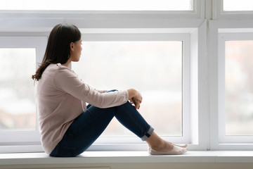 Fototapeta na wymiar Pensive biracial woman sit on windowsill thinking
