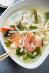 Close-up of panasian noodle soup with wontons and shrimps, selective focus