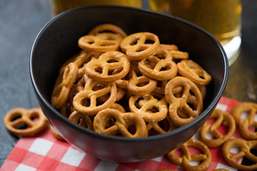 Close-up of a black bowl with pretzels and beer mugs in the background, studio shot, selective focus