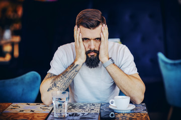 Young desperate bearded tattooed muscular handsome hipster holding hands on face and looking at...