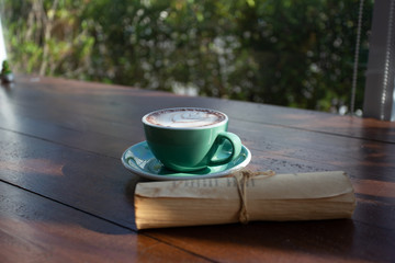 A green cup of coffee placed on a wooden table by the window in a coffee shop, Concept: Delicious breakfast drinks fragrant suitable for lifestyle, closeup cup of coffee over the top with space