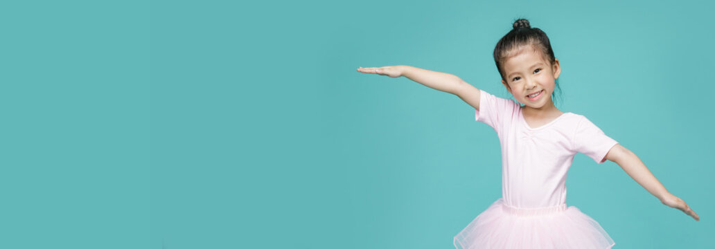 Beautiful smiling Asian little girl in a pink suit is dancing a ballet at school, empty space in studio shot isolated on colorful blue long banner background