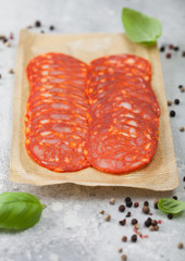 Pack of dry-cured chorizo sausage slices with a distinctive spicy paprika flavour with basil and pepper on light kitchen table background.
