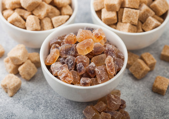 White ceramic bowl plates of natural brown unrefined and caramelized sugar cubes on light table background.