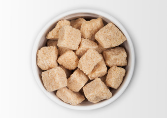 Glass bowl plate of natural brown unrefined sugar cubes on white background.