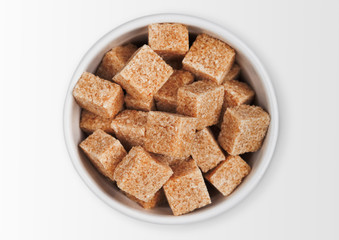 Glass bowl plate of natural brown sugar cubes on white background.
