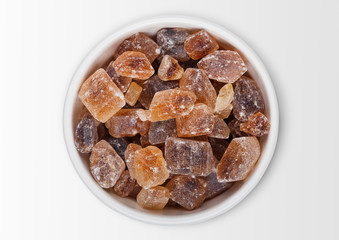 Glass bowl of natural brown caramelized sugar cubes on white background.