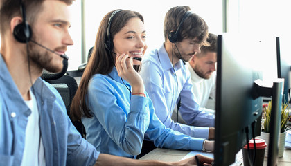 Portrait of call center worker accompanied by her team. Smiling customer support operator at work. - obrazy, fototapety, plakaty