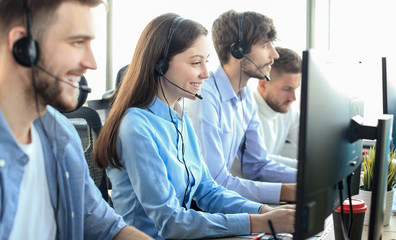 Portrait of call center worker accompanied by her team. Smiling customer support operator at work.