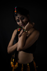 Fashion portrait of a Indian Bengali brunette woman in Indian traditional tribal/ villager dress and handmade ornaments in dark copy space studio background. Indian lifestyle and fashion photography.
