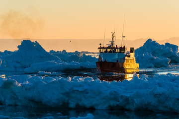 Fishing boat navigates glacier-filled waters at sunset. Greenland © Mikael