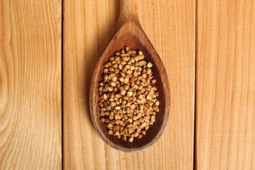 Buckwheat groats on wooden spoon at plank background. Directly Above.