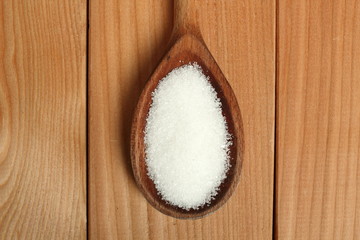 Sugar on wooden spoon at plank background. Directly Above.